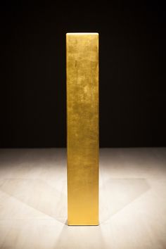 a tall gold object sitting on top of a white floor next to a black wall