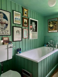 a bathroom with green paneling and pictures on the wall above the bathtub is shown