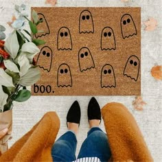 a person standing in front of a door mat with ghost faces on it and flowers