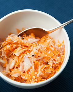 a white bowl filled with shredded carrots on top of a blue table cloth next to a silver spoon