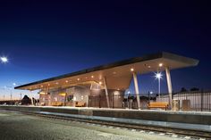 an empty train station at night with lights on the roof and benches along the tracks