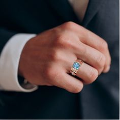 a man in a suit and tie wearing a gold ring with a blue topaz