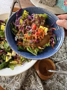 a salad with dressing in a blue bowl on a white plate next to a brown sauce