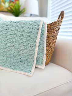 two blue crocheted blankets sitting on top of a white couch next to a basket