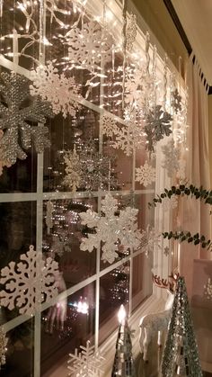 snowflakes are hanging on the window sill in front of a christmas tree