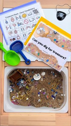 there is a sand tray with some toys in it and an open book on the table