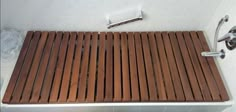 a wooden shower mat sitting on top of a bath tub next to a faucet