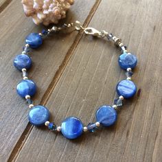 a bracelet with blue glass beads on a wooden table next to a rock and seashell