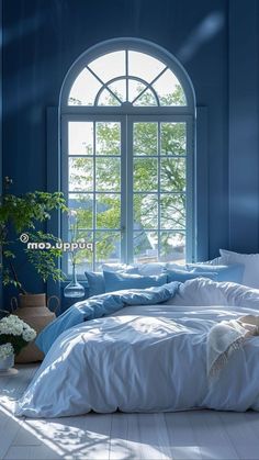 a bedroom with blue walls and white bedding in front of a large arched window