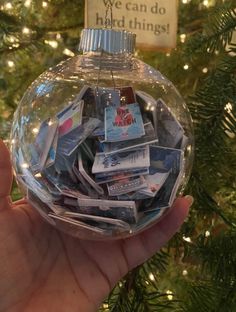 a hand holding a glass ornament filled with cards and christmas tree lights in the background