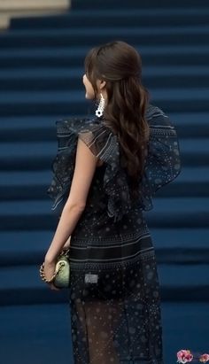 a woman with long hair wearing a black dress and holding a green purse in her hand