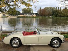 an old fashioned sports car is parked by the water