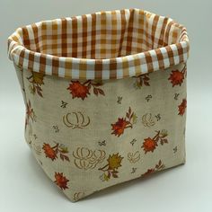 a fabric basket with autumn leaves and monogrammed letters on the front, sitting on a white surface