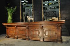 a large wooden desk sitting next to a tall plant in front of two windows with stained glass panes