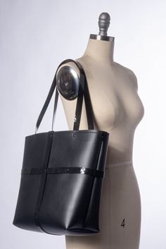 The Harness Tote Bag is the perfect sized every large tote bag for running around and doing all the things. Black vegan leather and shiny black PVC pair nicely together for a pleasing black-on-black texture contrast. PVC harness strap details form an "X" cage design around the body of the bag. Snap Closure at the top keeps all the goods inside. Nice sized handles for carrying or slinging over one's shoulder. Black hardware. Lined in strong black sport nylon with a tiny inner pocket. BAG DIMENSIO Texture Contrast, Black Minimal, Black Pvc, Black Vegan, Black Textures, Black Hardware, Large Tote Bag, Black Tote Bag, Large Tote