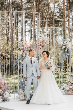 a bride and groom standing in front of an outdoor wedding ceremony arch with floral arrangements