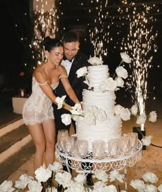 a newly married couple cutting their wedding cake at night with sparklers in the background