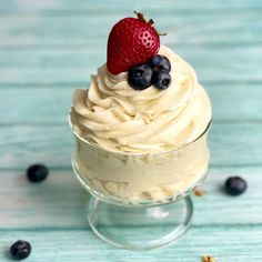 a cupcake with whipped cream and fresh berries on top is sitting in a glass dish