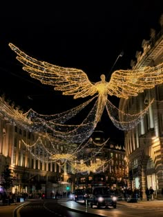 an angel statue is lit up in the night sky above a city street with cars and buildings