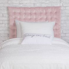 a bed with white pillows and blue headboard against a brick wall in a bedroom