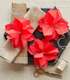 red paper poinsettis are sitting on a black plate next to twine spools