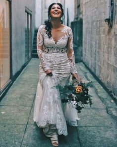 a woman in a wedding dress is walking down the street holding a bouquet and smiling