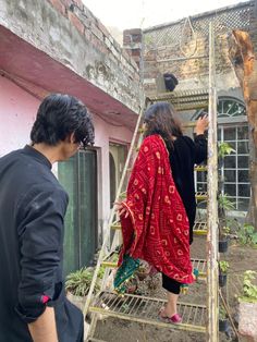 two people are standing on a ladder in front of a pink building and one person is wearing a red robe