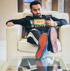 a man sitting in a chair with his feet up on the glass table and holding a cell phone