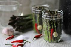 three glass jars filled with green and red vegetables next to garlic, pepper, and onion