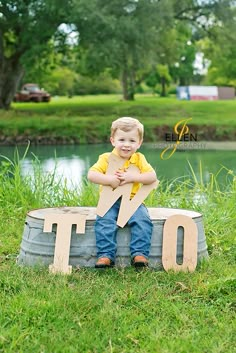 a young boy sitting on top of a wooden sign in the grass near a pond