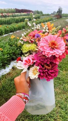 a person holding a bag full of flowers in their hand on the grass near some water