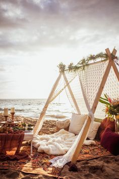 a bed on the beach is set up with pillows, blankets and other things to decorate