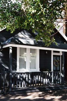 a small black house with white trim and shutters on the front door is surrounded by trees