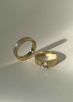 two gold wedding rings sitting next to each other on a white surface, with one diamond in the middle