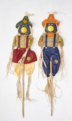 two scarecrows with hats and overalls on sticks