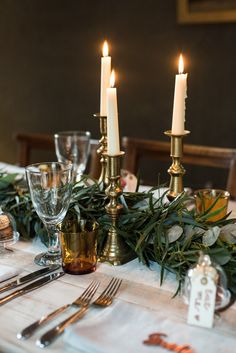 the table is set with silverware, candles and greenery for an elegant dinner