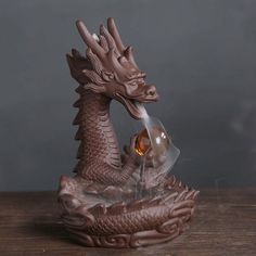 a statue of a dragon with an orange stone in its mouth on a wooden table