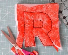 scissors are laying next to an orange piece of fabric with the letter r on it