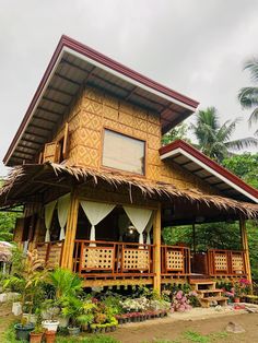 a wooden house with thatched roof and white drapes on the windows is surrounded by greenery