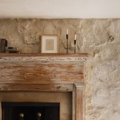 a fireplace in a stone walled room with candles and pictures on the mantel above it