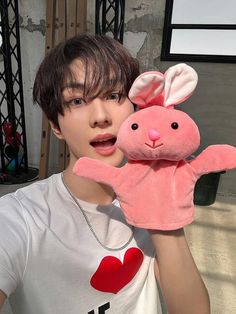 a person holding a pink stuffed animal in front of their face and wearing a white t - shirt