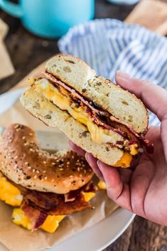 a person is holding up a sandwich with bacon and cheese on it, next to a bagel