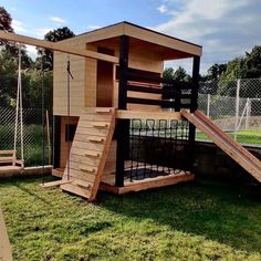 a small wooden play house with stairs and slide on the grass in front of it