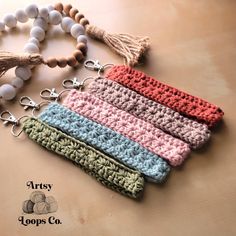 four crocheted key chains with tassels and beads on a wooden table