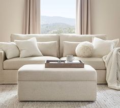 a living room with a couch, ottoman and window overlooking the mountains is shown in this image