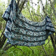 a blue and black shawl hanging from a tree in the woods with green grass