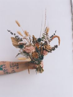 a person's arm with tattoos holding a bouquet of flowers and plants in it