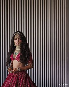 a woman in a red and gold lehenga poses for the camera with her hands on her hips