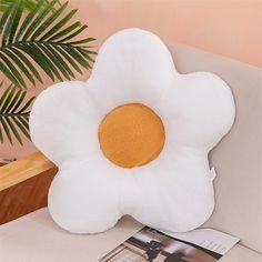 a white flower shaped pillow sitting on top of a table next to a potted plant