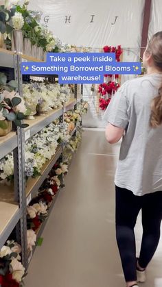 a woman is walking down the aisle in a flower shop with flowers on shelves behind her